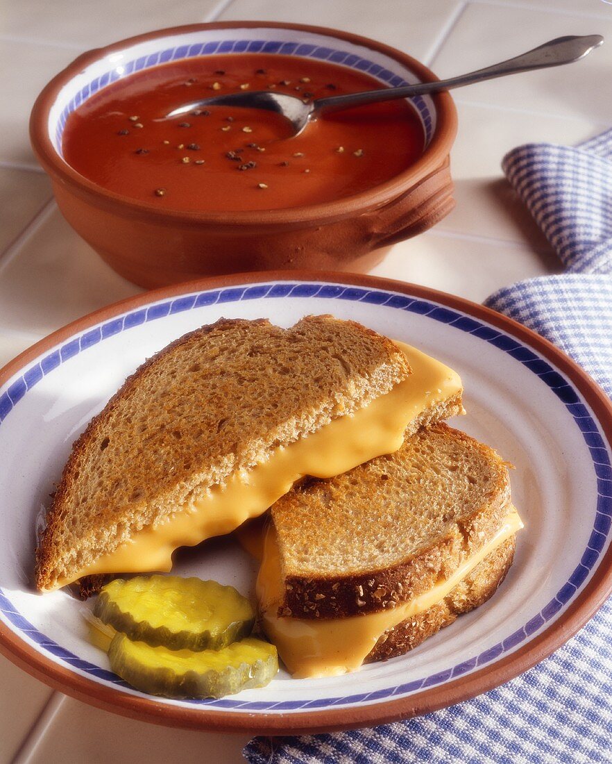 A Grilled Cheese Sandwich with Two Pickle Slices and Tomato Soup