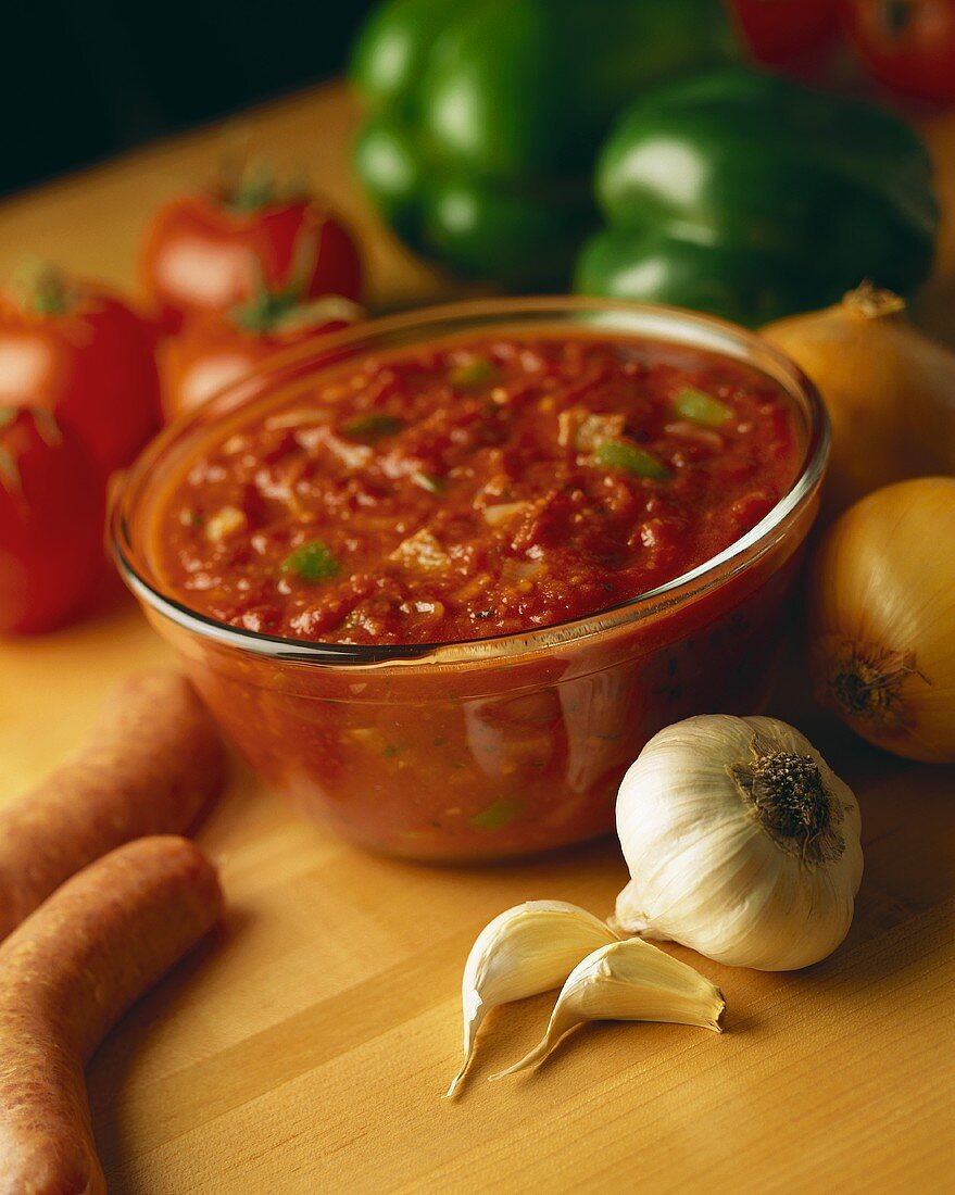 Tomato salsa in glass bowl; fresh vegetables; sausages