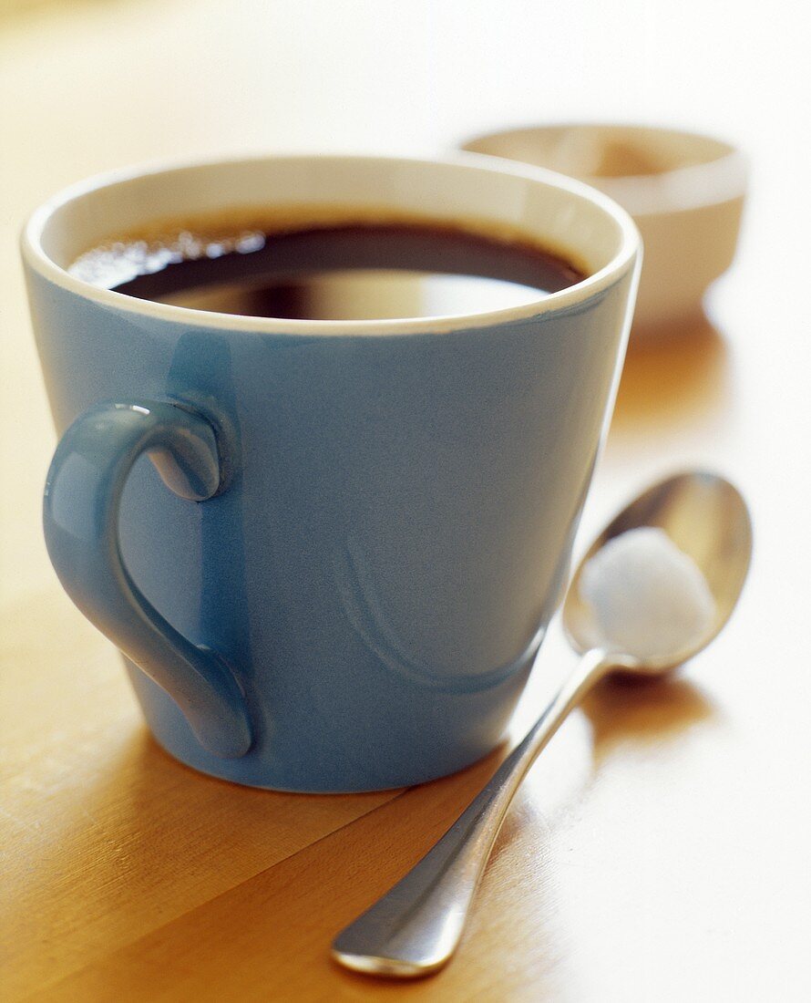Schwarzer Kaffee in blauer Tasse mit Löffel und Zuckerwürfel