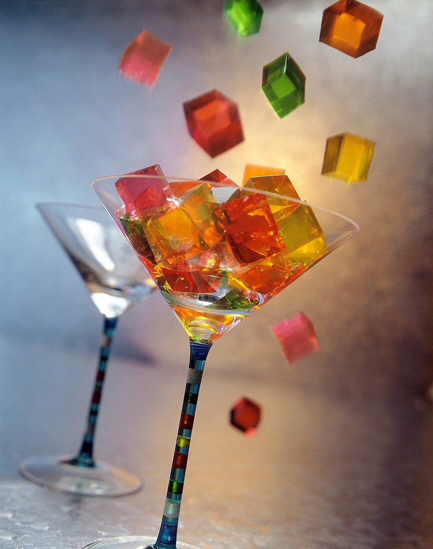 Bunte Geleewürfel fallen in ein Cocktailglas