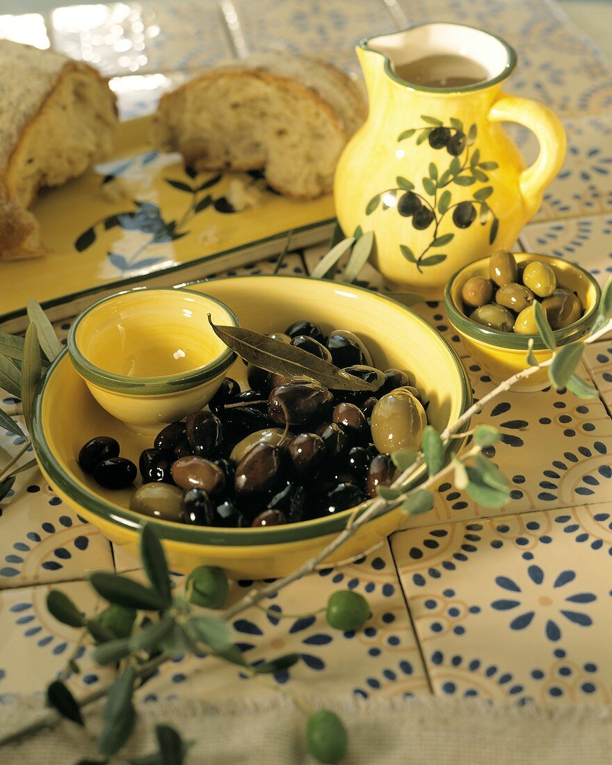Eingelegte Oliven in mediterranem Geschirr; Olivenöl; Brot