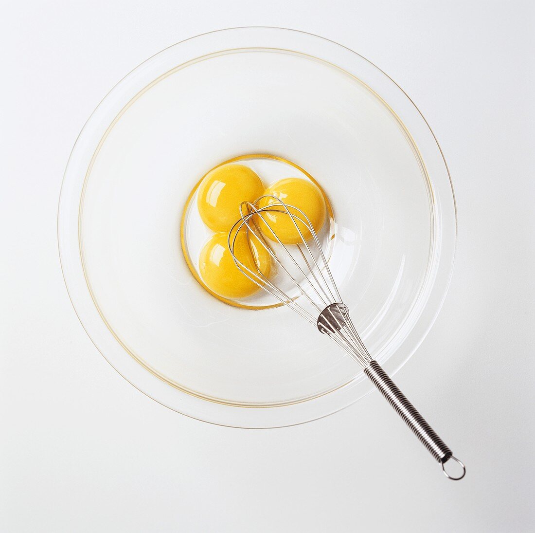 Three Egg Yolks in a Bowl with a Whisk