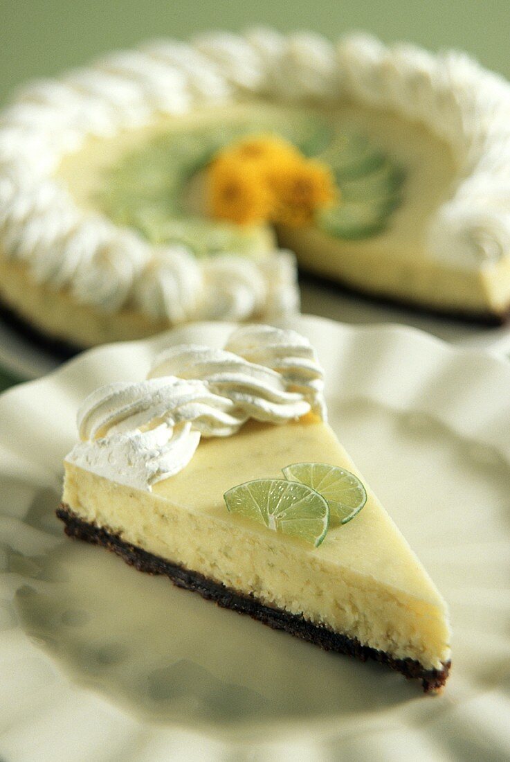 Stück Key Lime Cheesecake auf Teller, dahinter ganzer Kuchen