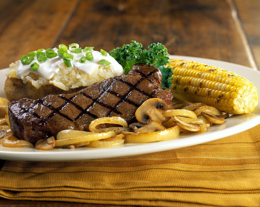 Barbecued beef steak with baked potato and corncob