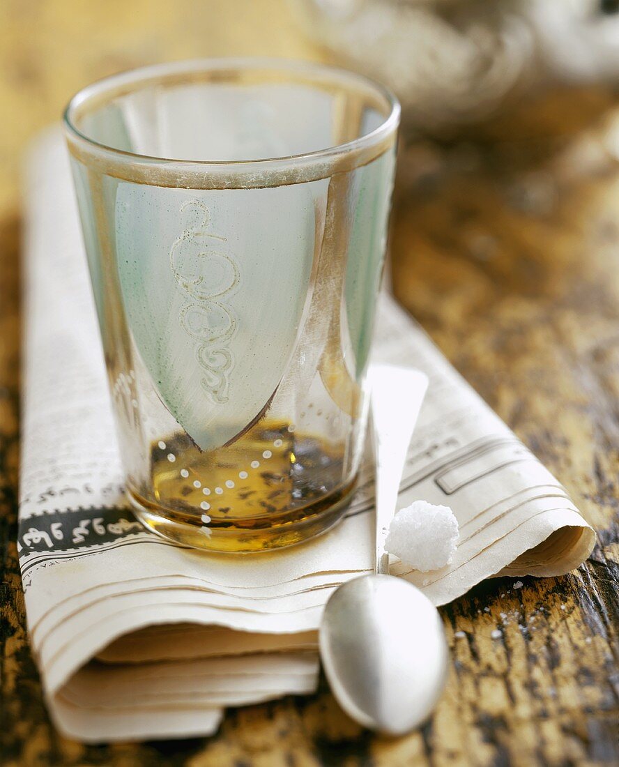 A tea glass with tea leaves on a newspaper