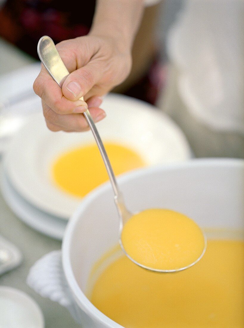 A hand serving butternut squash soup from a stockpot