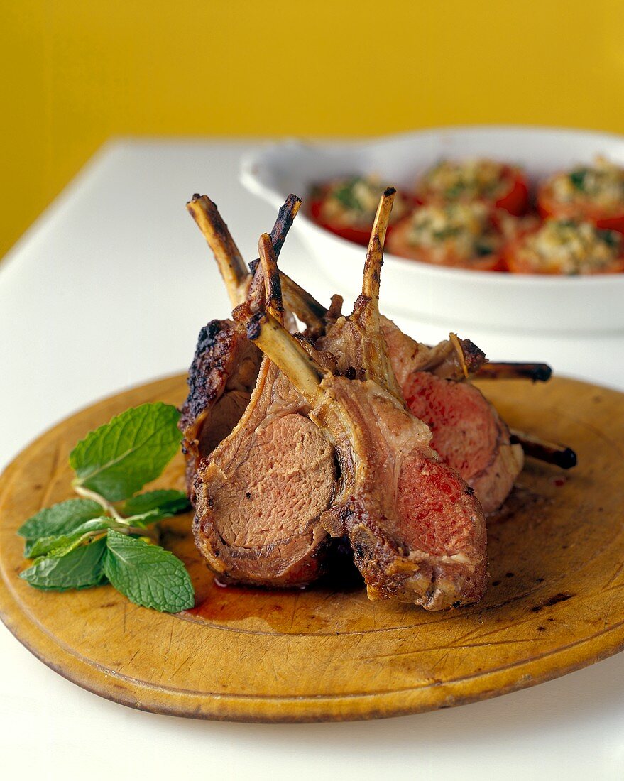 Fried lamb cutlets on wooden plate; stuffed tomatoes