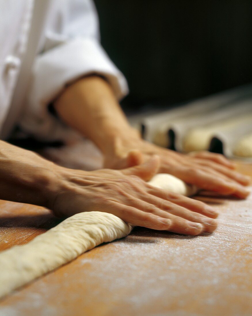 Baker rolling out baguette dough