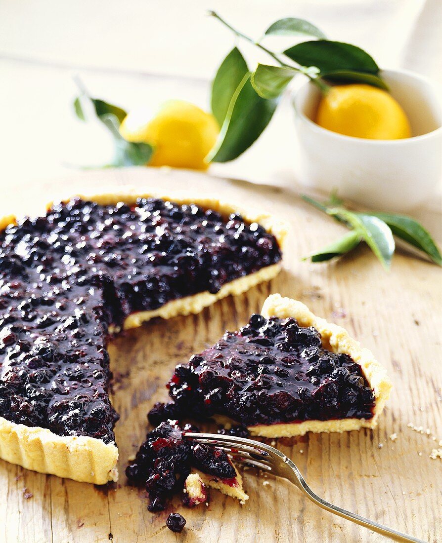 Stück Heidelbeertarte vor angeschnittener Torte