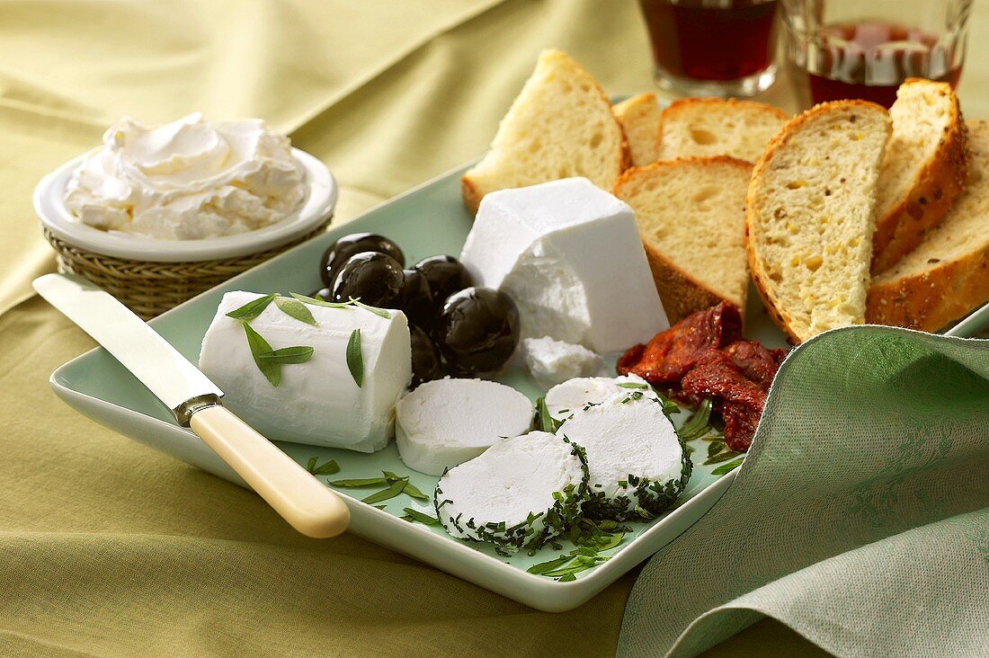 Platte mit Ziegenfrischkäse, Brotscheiben, Oliven etc.