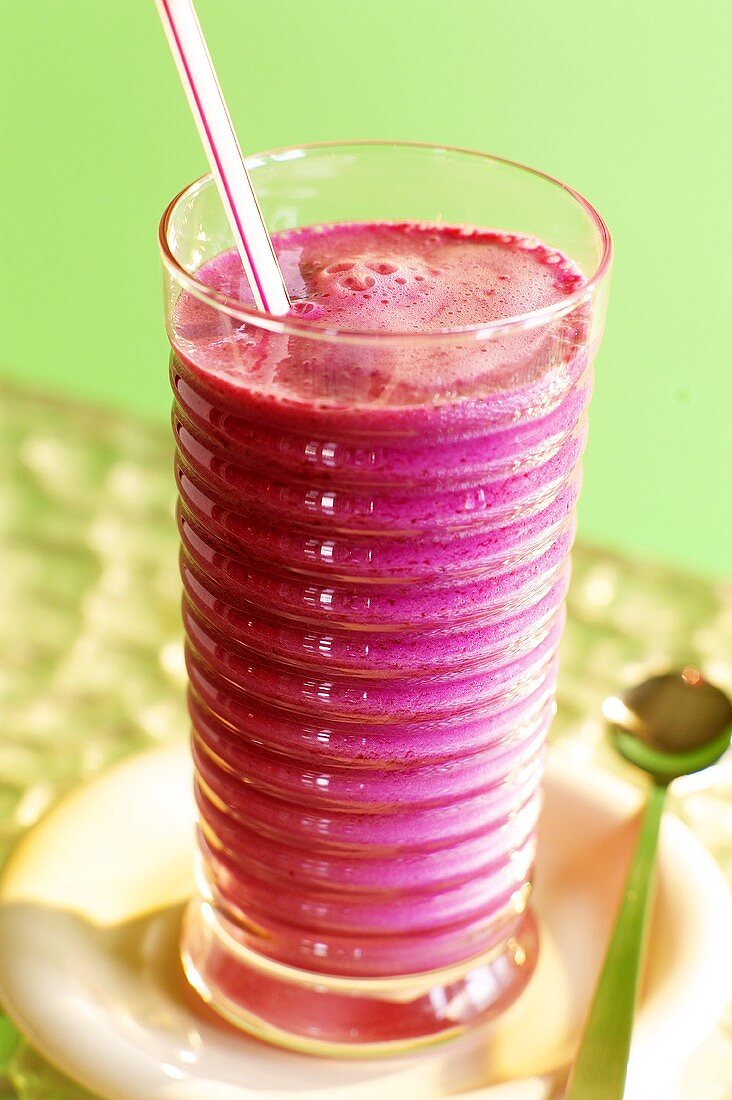 Raspberry smoothie with straw against green background