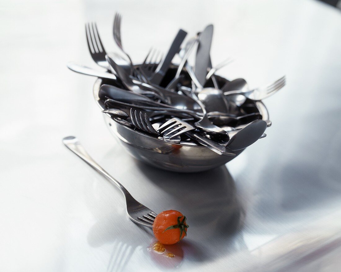 A cherry tomato on fork in front of bowl with cutlery