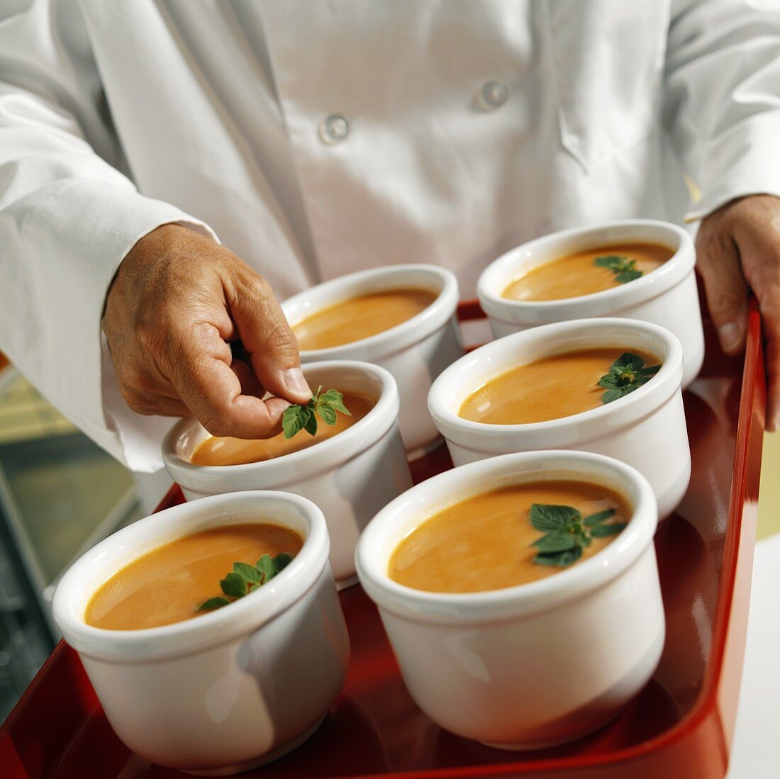 A Chef Placing Oregano Garnish on Bowls of Tomato Soup