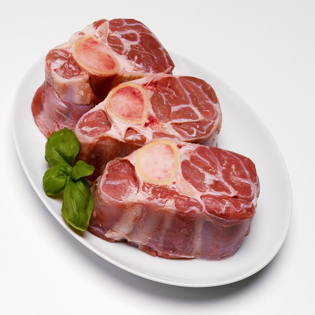Three Raw Chops for Osso Bucco with Basil on White