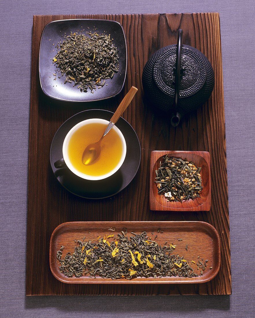 Cup of green tea, teapot and various types of tea leaves