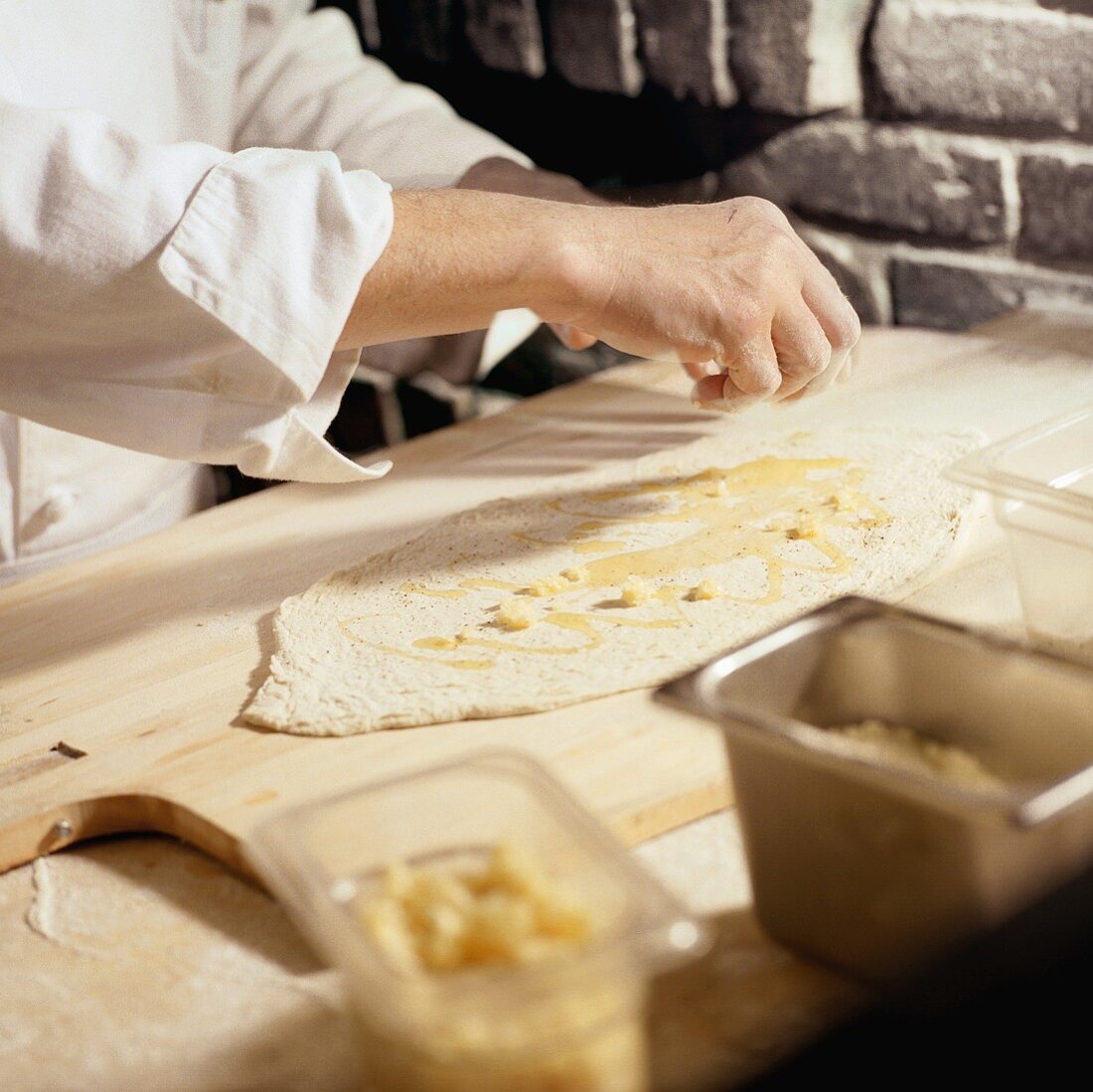 Chef Placing Small Pieces of Cheese on Rolled Out Pizza Dough