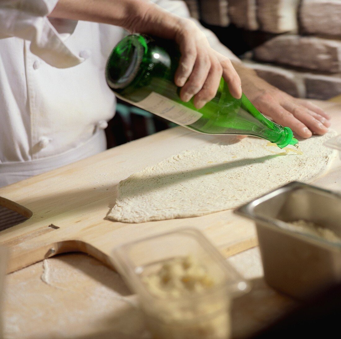 Chef Pouring Oil From Bottle onto Rolled Pizza Dough