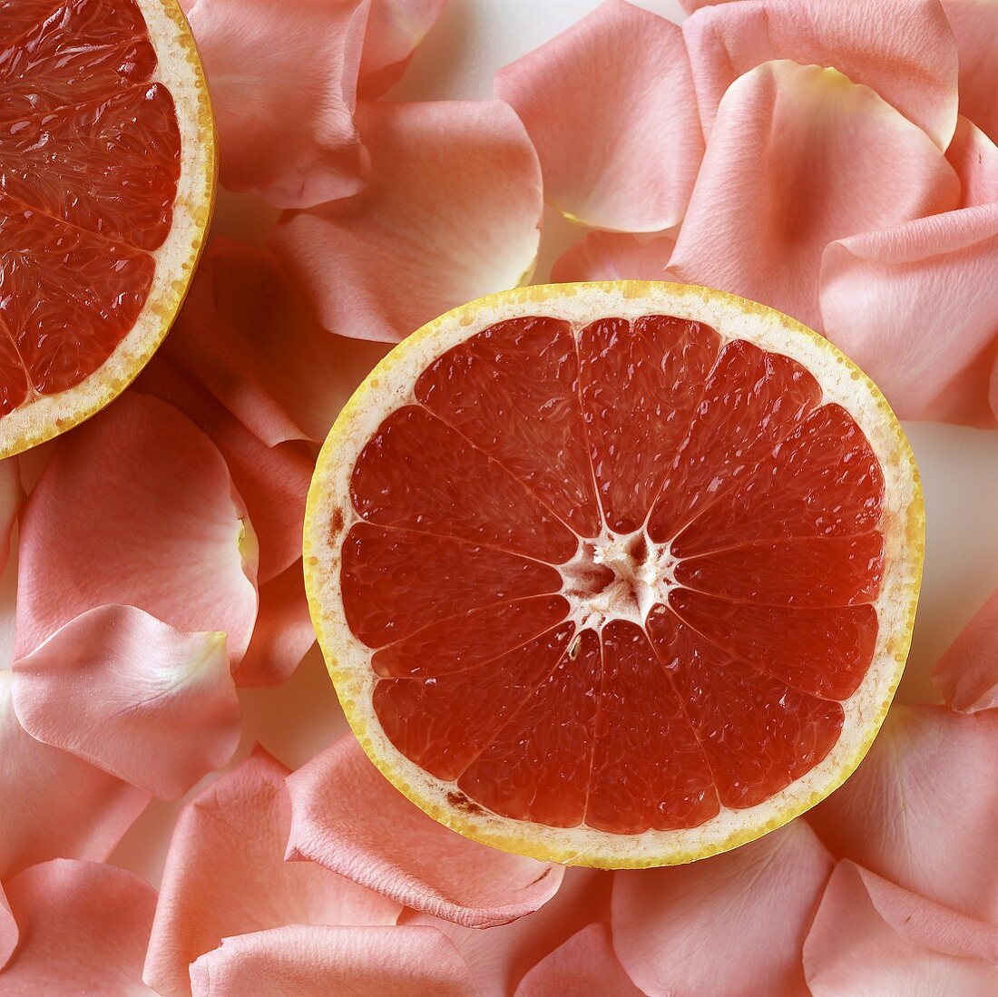 Halbierte Grapefruit auf rosafarbenen Rosenblättern