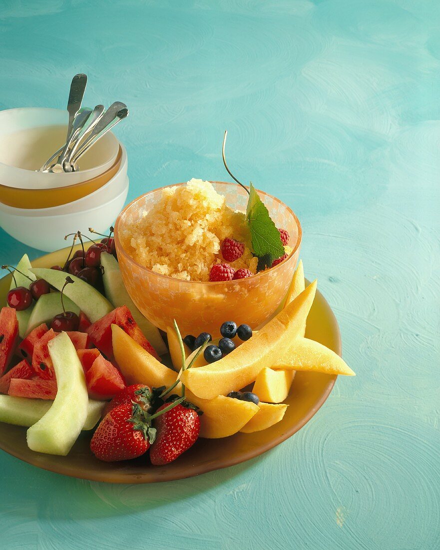 A Bowl of Cantaloupe Granita on a Platter with Fresh Melon Wedges and Berries