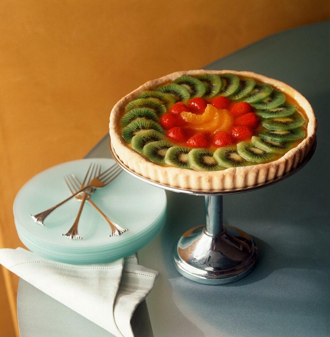 Fruit tart with kiwis, strawberries & oranges on cake stand 
