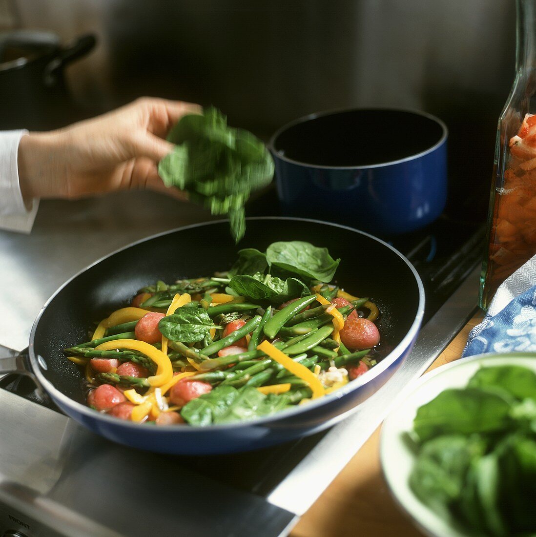 Adding spinach to vegetables in a frying pan
