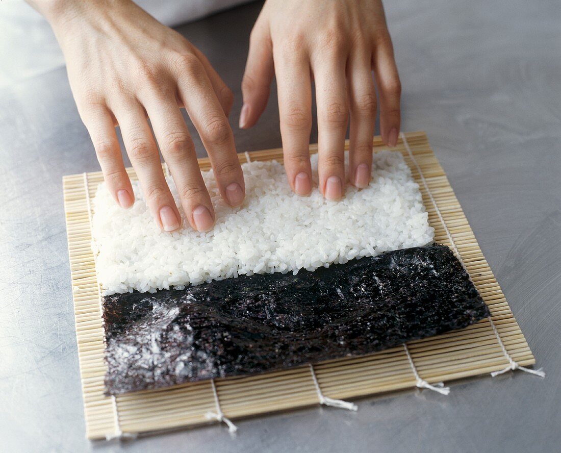 Making Maki Sushi: Hands Pressing Rice onto a Sheet of Nori