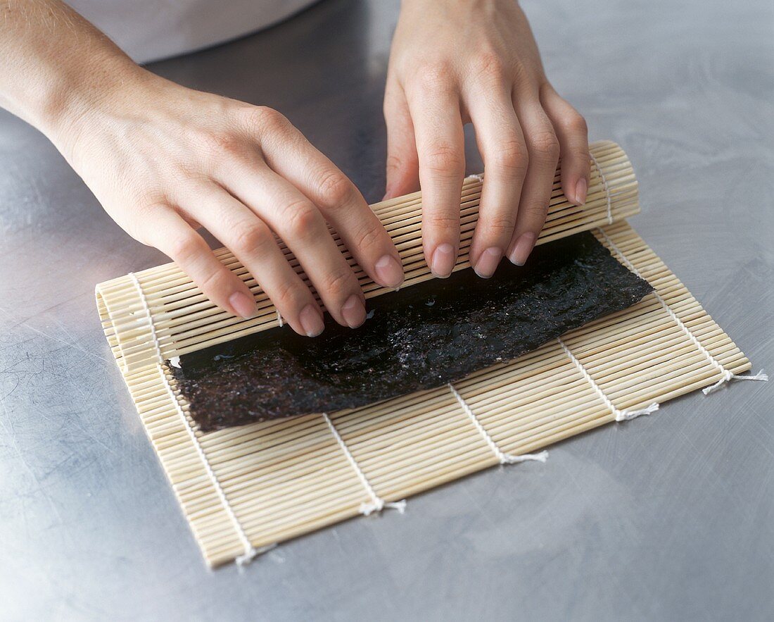 Maki-Sushi zubereiten: Noriblatt mit Bambusmatte aufrollen