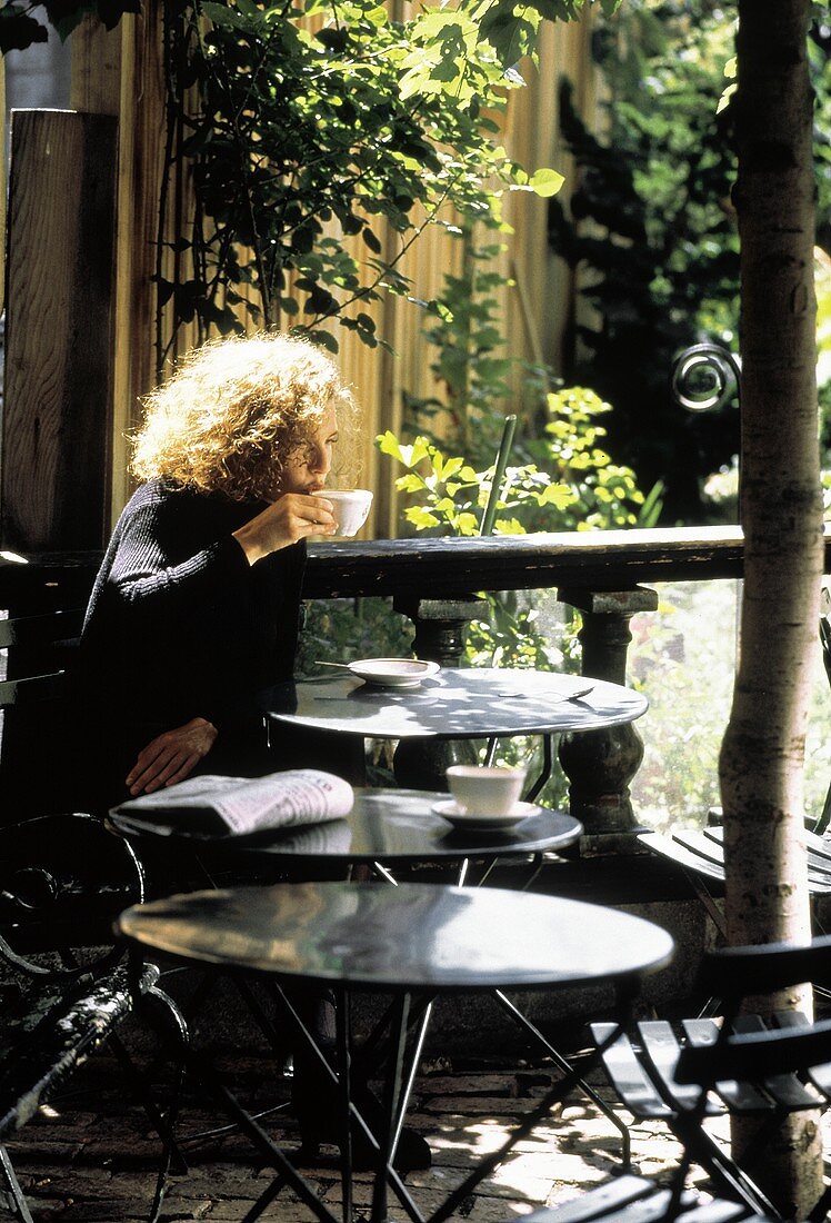 Frau trinkt Kaffee in sonnigem Gartencafe