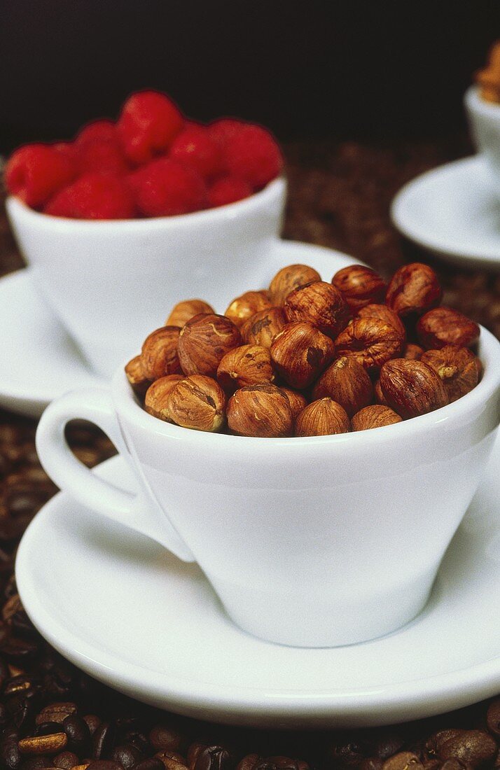 Haselnüsse in einer Tasse vor Himbeeren in einer Tasse