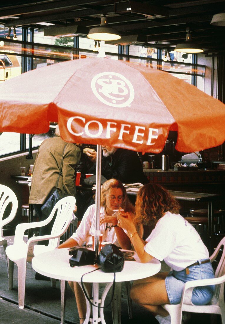 Zwei Frauen sitzen an einem Tisch mit Sonnenschirm in Café