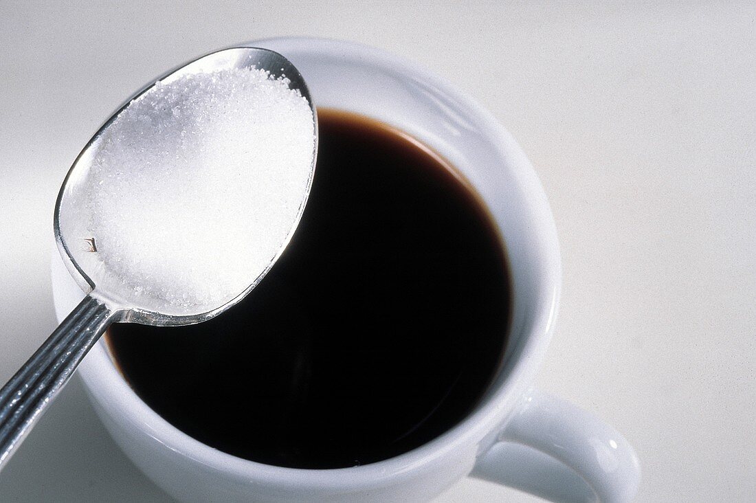 Ein Löffel mit Zucker über einer Kaffeetasse