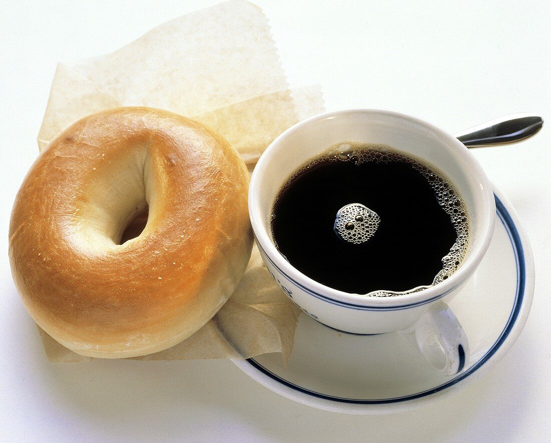Ein Bagel auf Papier & eine Tasse schwarzer Kaffee