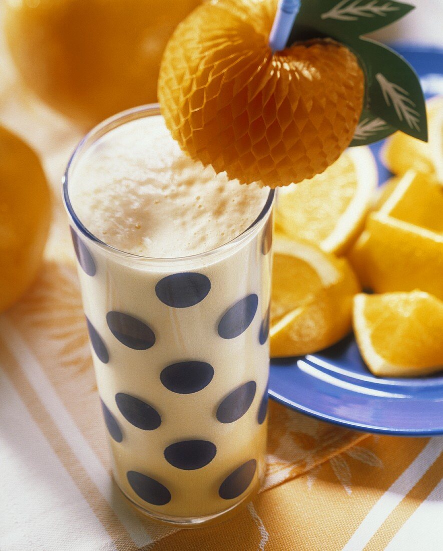 Orangen-Milchshake im Glas, daneben Orangenstücke
