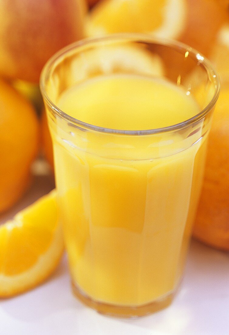 Ein volles Glas Orangensaft vor Orangen