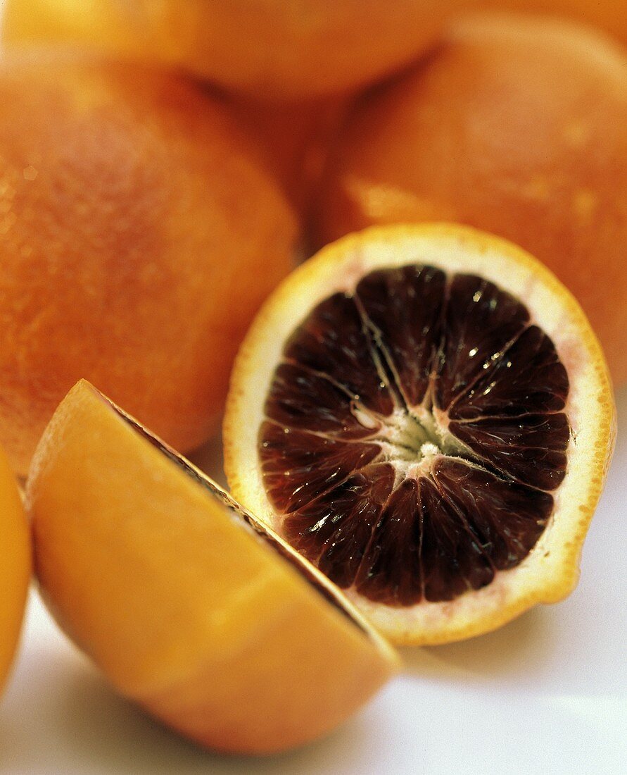 Blutorange, in zwei Hälften geschnitten, vor ganzen Orangen