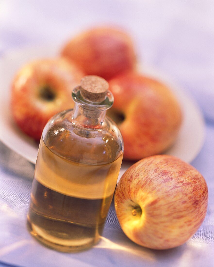 Apfelessig in Flasche neben Gala Apfel; Äpfel auf Teller