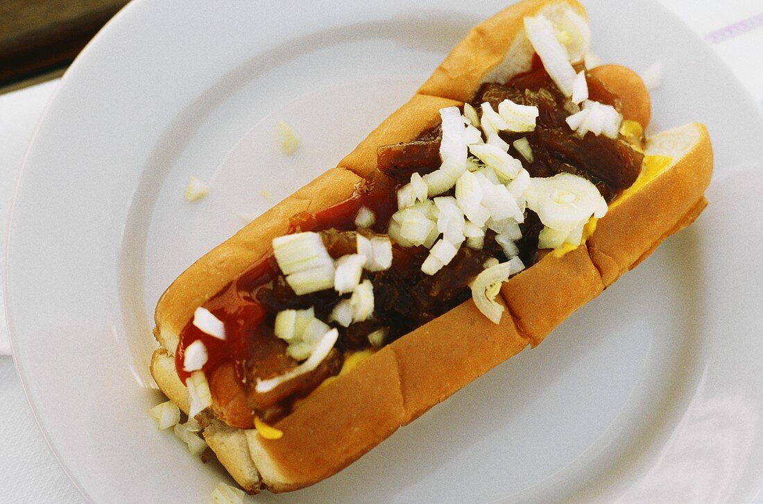 Hot Dog mit Gewürzsauce, Ketchup & Zwiebeln auf Teller