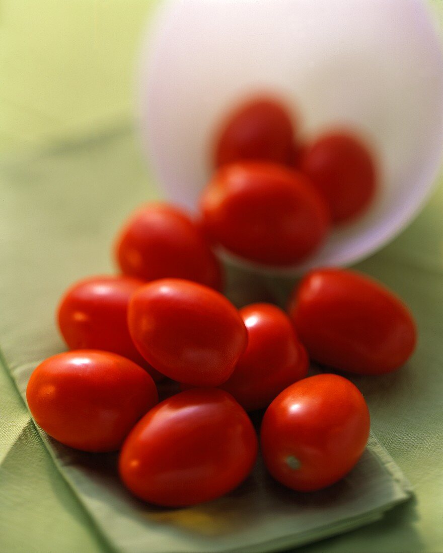 Mehrere Eiertomaten auf grünem Tuch und in einer Schale