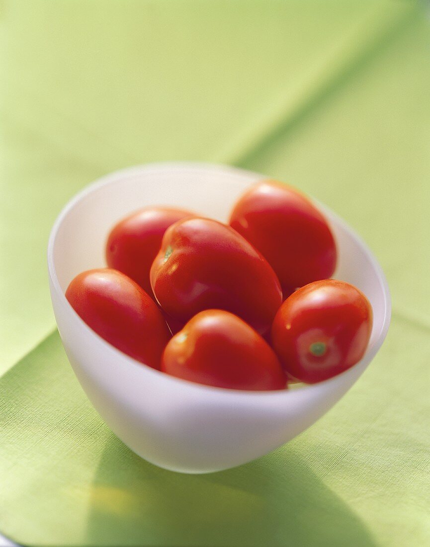 Mehrere Eiertomaten in weisser Schale auf grünem Tuch