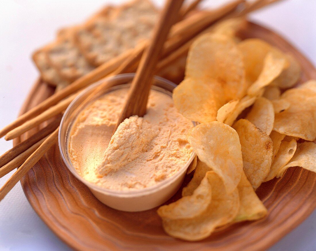 Cheese dip with crisps, salted sticks & crackers on wooden board