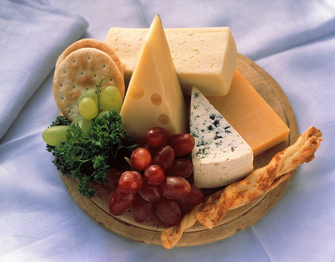 Verschiedene Käsesorten auf Holzteller mit Trauben, Crackern