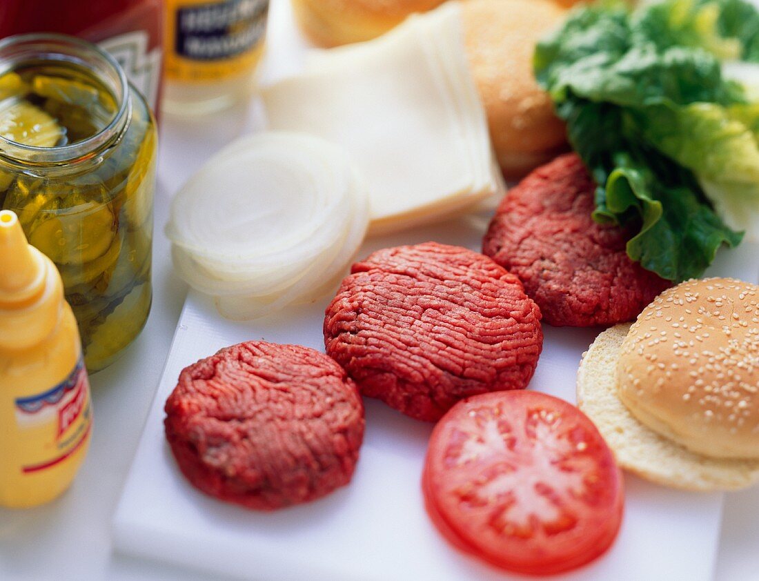 Zutaten für Burger: rohe Frikadellen, Käse, Gemüse etc.