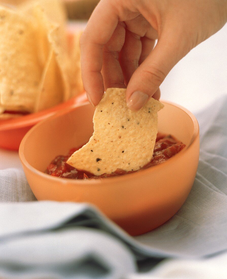 A Hand Dipping a Chip into a Bowl of Salsa