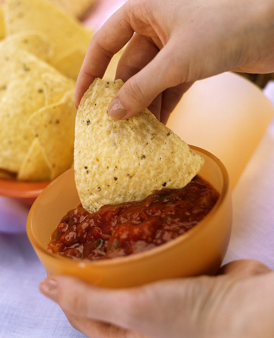 Hand Dipping a Chip into a Bowl of Salsa