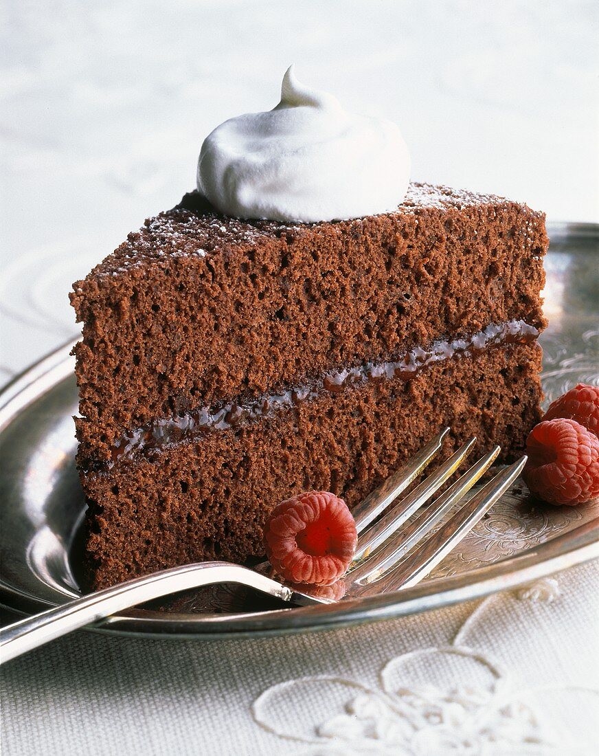Ein Stück Schokoladenkuchen mit Sahnetupfen & Himbeeren
