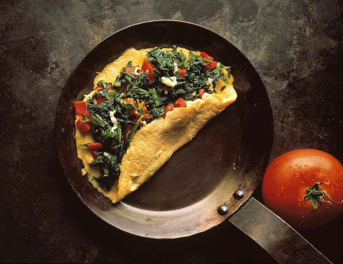 Omelett belegt mit Spinat und Tomatenwürfeln in einer Pfanne
