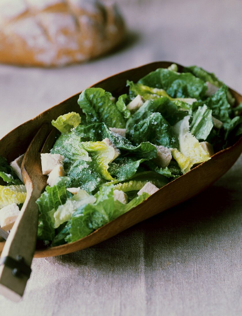 Cäsarsalat mit Putenfleisch in einem Holzgefäss mit Holzgabel