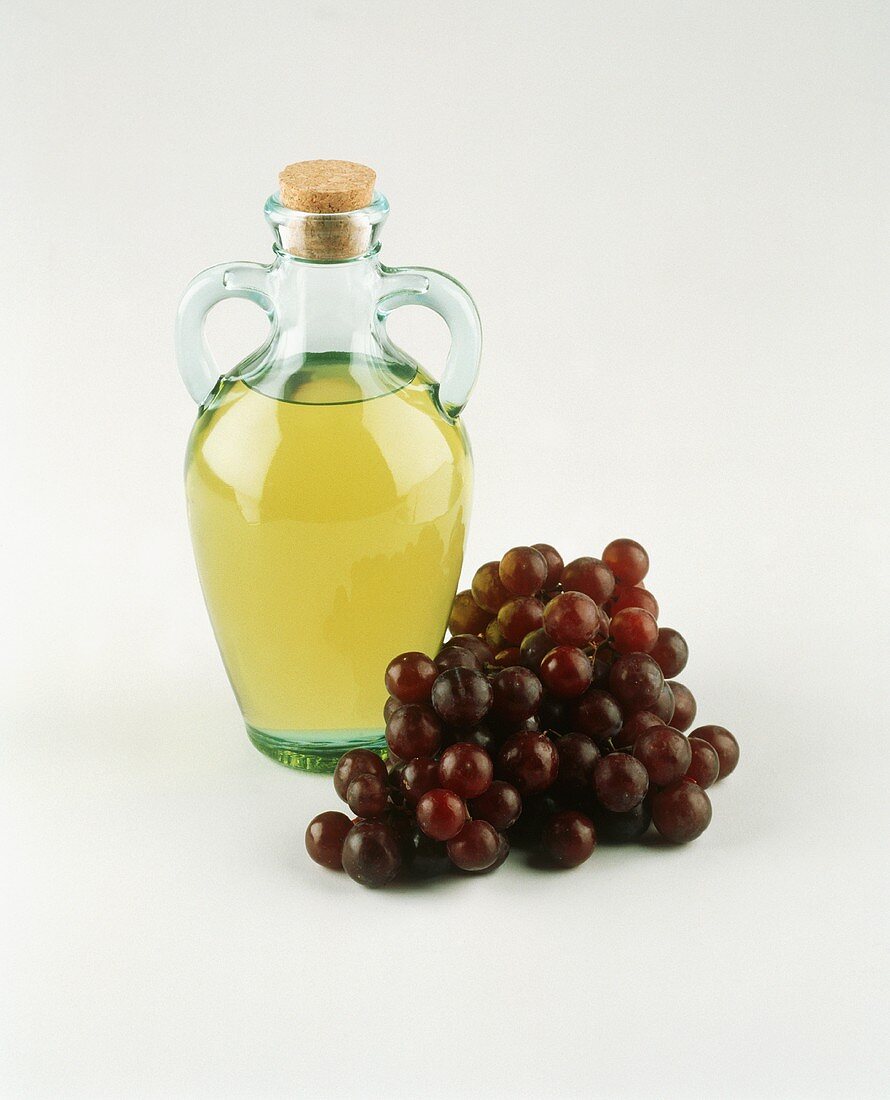 Eine Flasche Öl, daneben rote Trauben