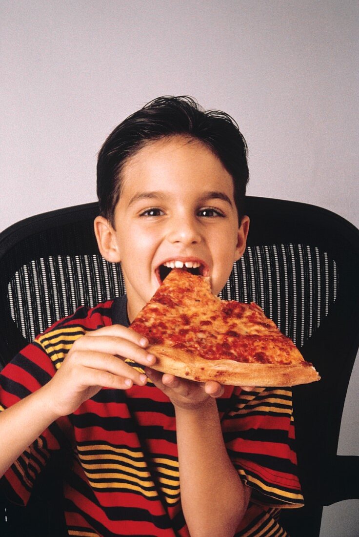 Kleiner Junge will gerade in ein grosses Stück Pizza beissen