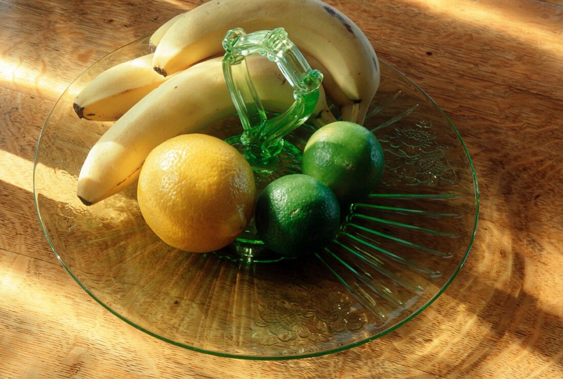 Bananen, Zitrone und Limetten auf einem Glasteller